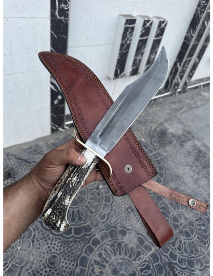 Handmade full tang carbon steel Bowie knife resting on brown leather sheath.