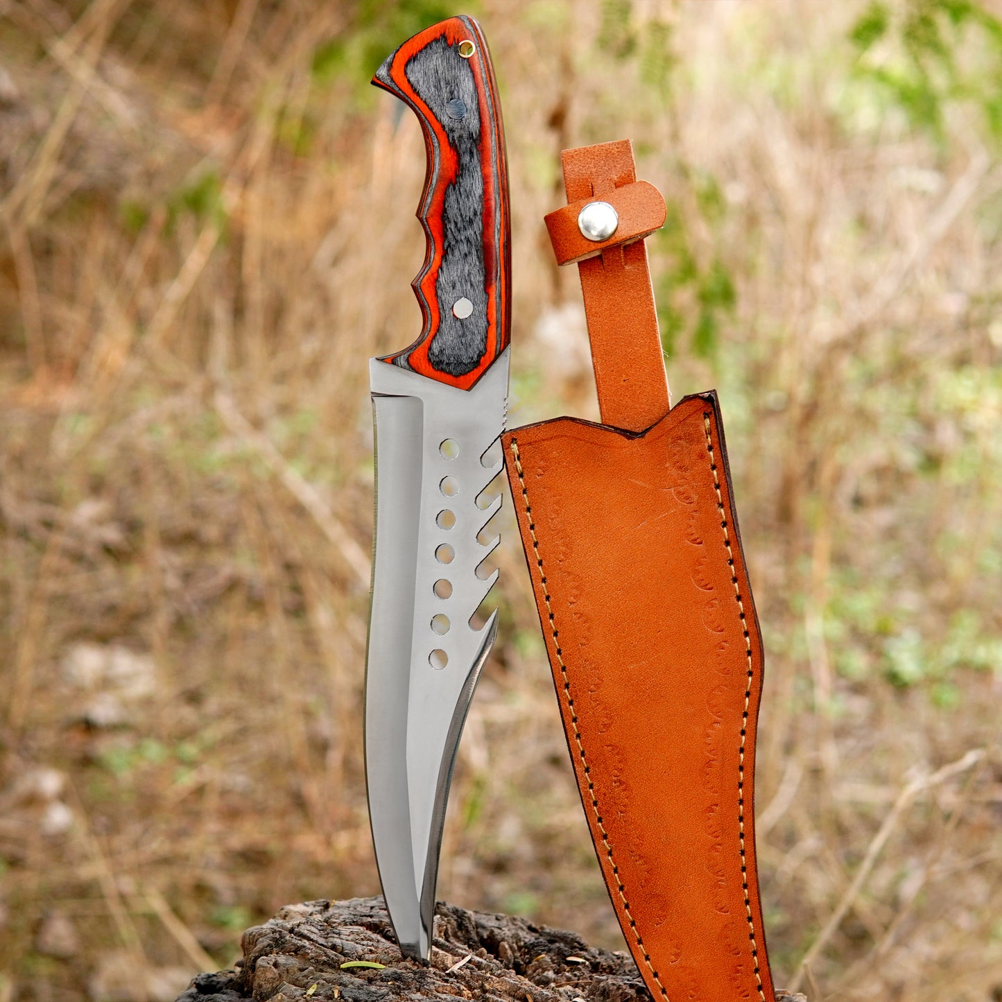 Handmade sawback bowie knife placed on a wooden stump outdoors featuring a sharp carbon steel blade with aggressive sawback spine and strong full tang build. The red and black layered handle offers a comfortable grip while the leather sheath ensures safe carry. Designed for camping hunting bushcraft and survival use.