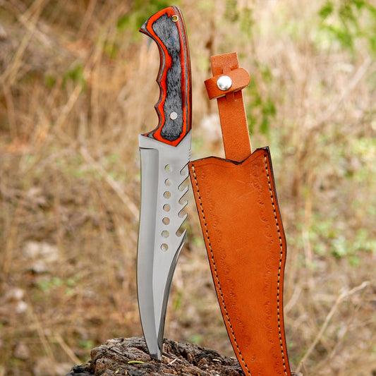 Handmade sawback bowie knife placed on a wooden stump outdoors featuring a sharp carbon steel blade with aggressive sawback spine and strong full tang build. The red and black layered handle offers a comfortable grip while the leather sheath ensures safe carry. Designed for camping hunting bushcraft and survival use.
