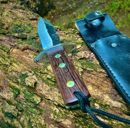 Outdoor display of full tang handmade hunting knife with polished wooden handle and black leather sheath.