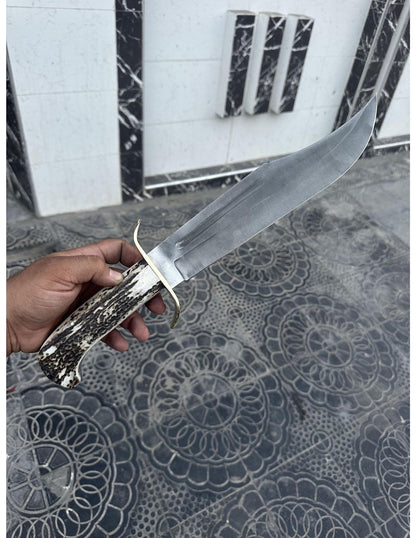 Full-length handmade Bowie knife with stag handle and leather sheath photographed outdoors.