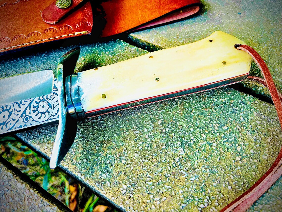 Close-up of natural material handle showing brass pins and red fiber liner details on engraved carbon steel bowie knife.
