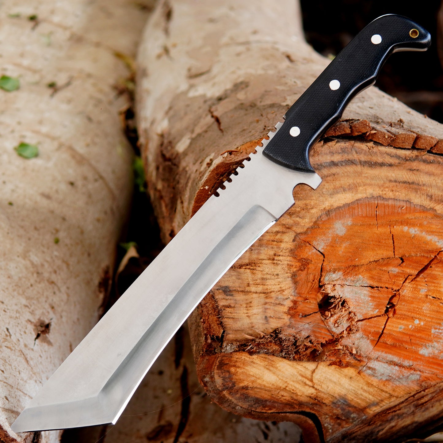 Close view of handmade bowie knife inside leather sheath placed on wooden background showing clean blade finish and durable sheath stitching designed for safe carry and outdoor use while maintaining traditional handcrafted appearance.