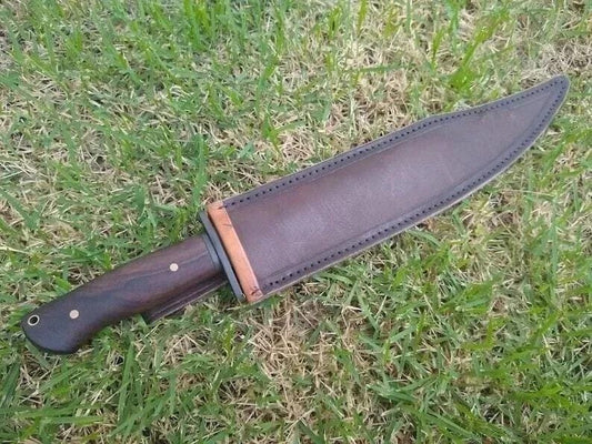 Bowie knife in leather sheath with rosewood handle lying on grass.