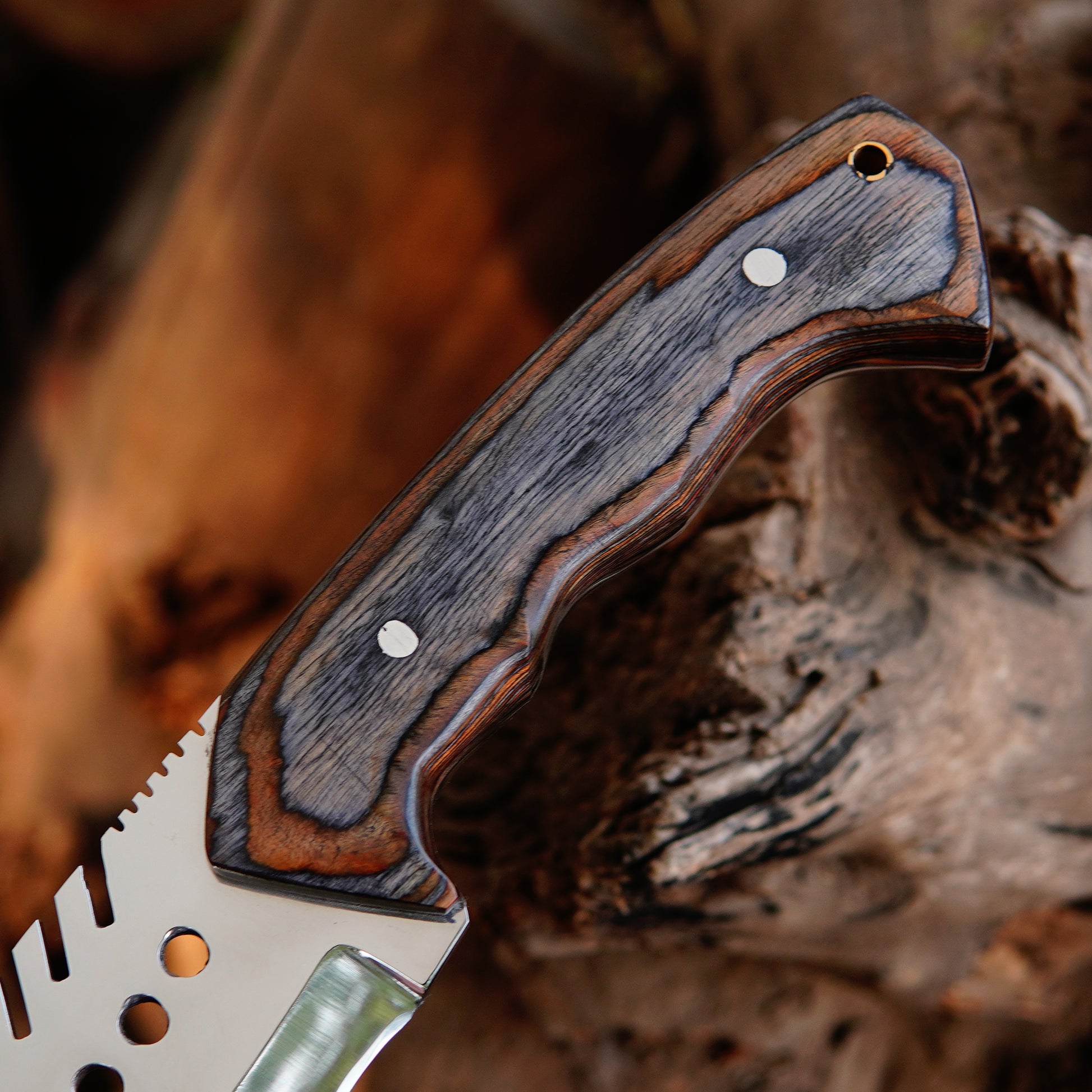 Handmade bowie knife photographed in an outdoor setting with natural background elements to emphasize its rugged use case. The image presents the knife as a dependable tool for outdoor enthusiasts, showing the full tang structure, comfortable grip, and protective leather sheath included with the product.