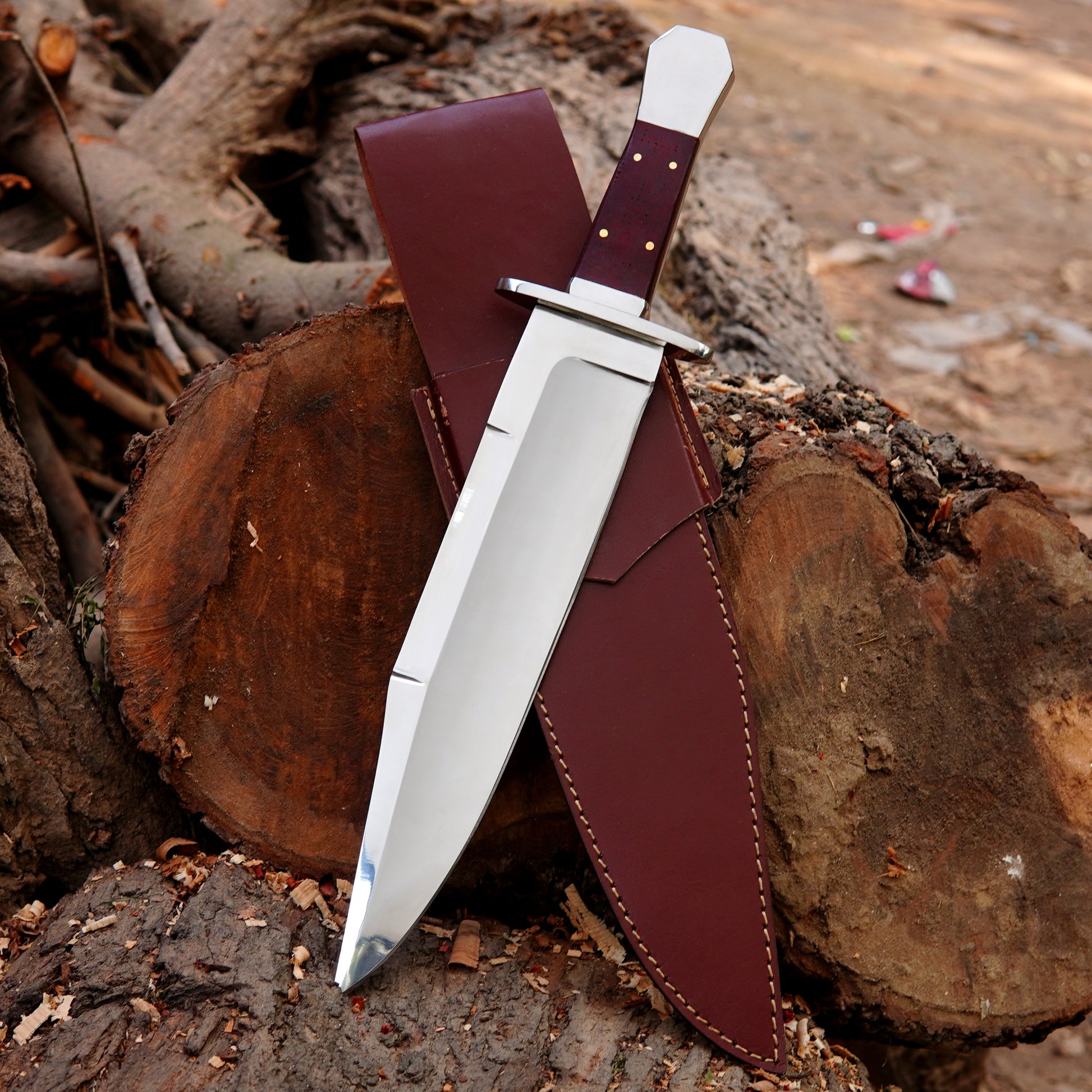 Handmade bowie style knife with polished steel blade, wooden handle, and premium leather sheath displayed on wood.