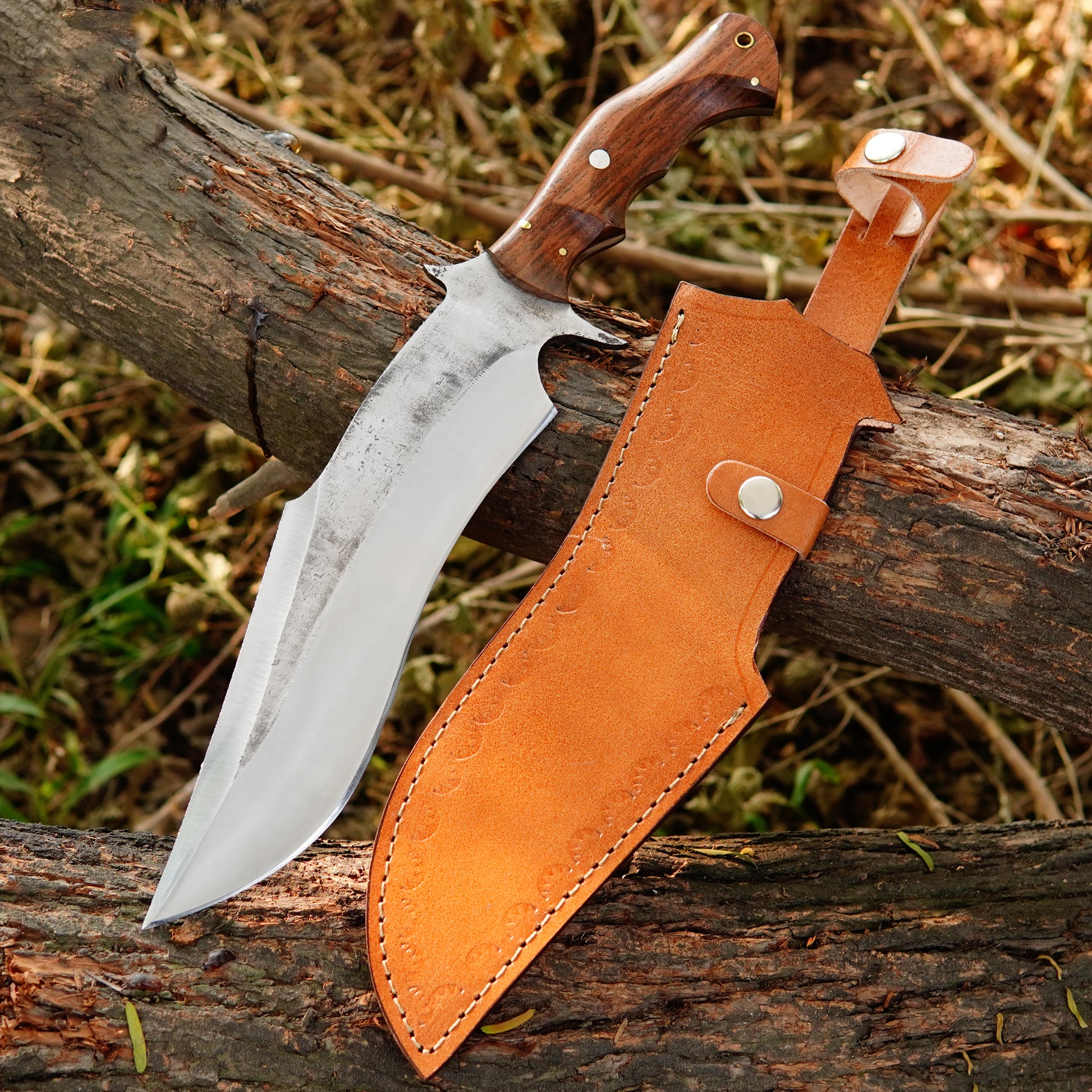 Handmade bowie style knife with polished steel blade, wooden handle, and leather sheath displayed on natural wood.
