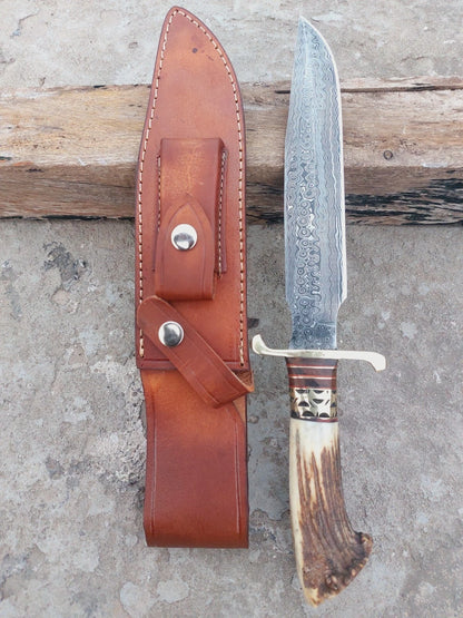 Damascus steel hunting knife with crown stag handle and brass spacers, showcasing traditional craftsmanship. A polished, sharp blade paired with a stitched leather sheath ensures safe storage and portability.