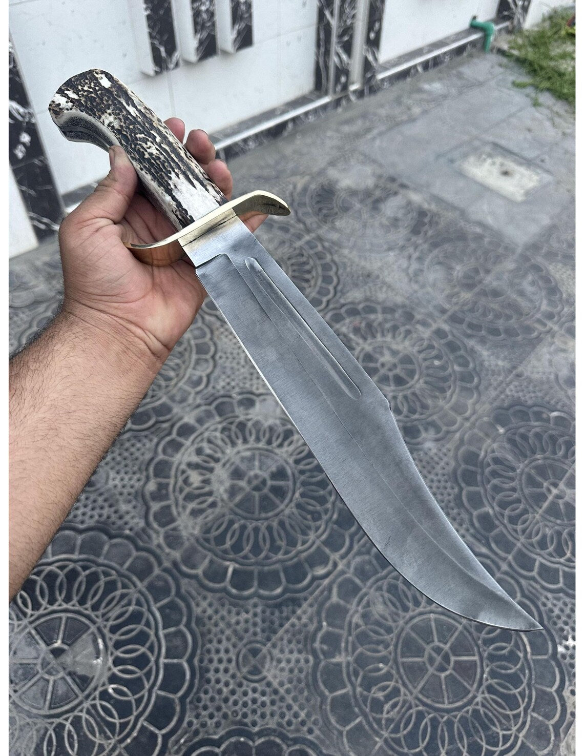 Handmade full tang Bowie knife with genuine stag handle and carbon steel blade held in hand.