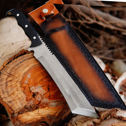 Handmade bowie knife displayed outdoors on natural wood surface showing full tang carbon steel blade and ergonomic handle design with leather sheath placed beside the knife highlighting craftsmanship and outdoor usability suitable for camping and collection purposes.