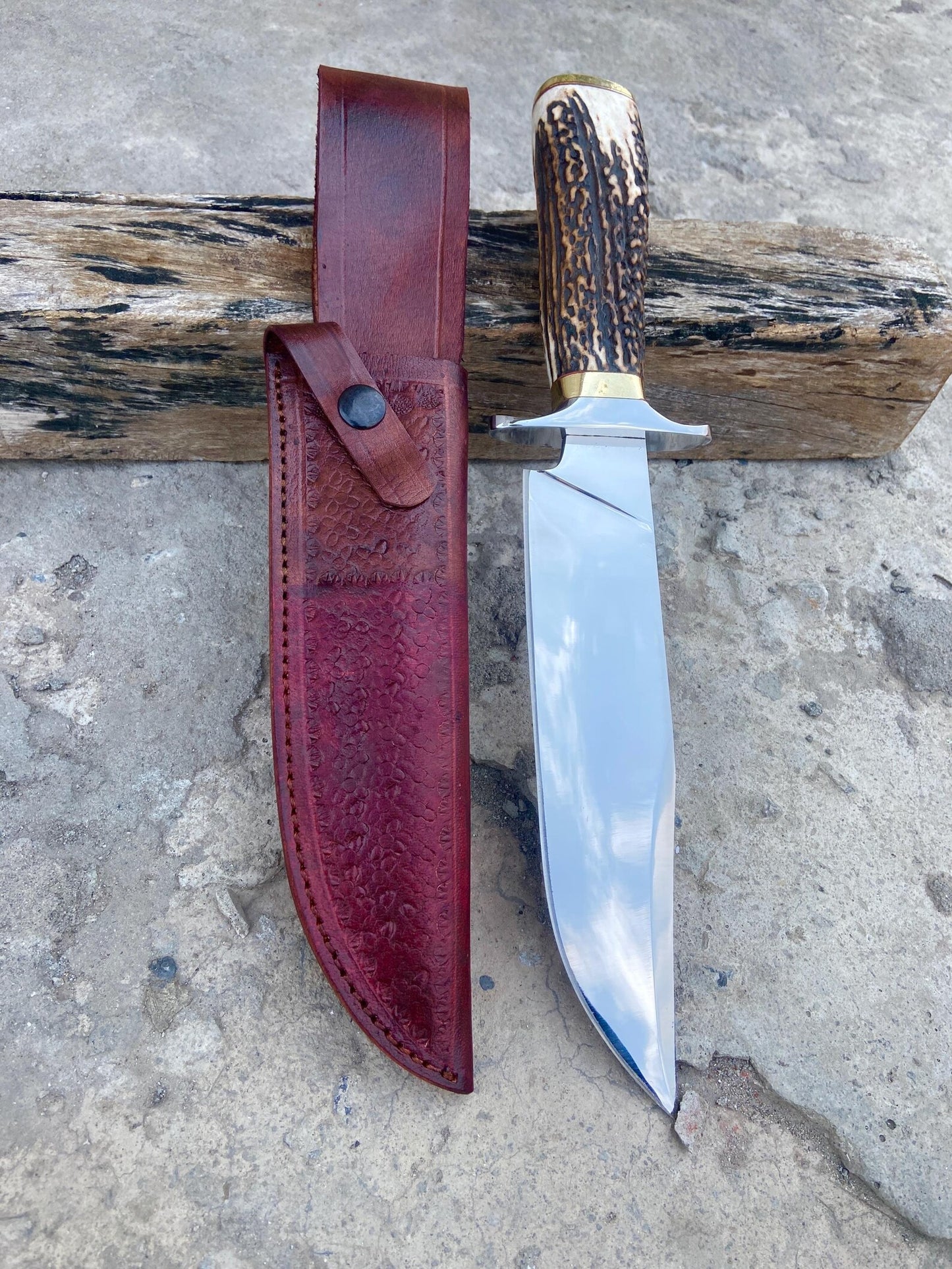 Handmade Bowie knife featuring a high-polished carbon steel blade and natural textured handle with brass fittings, displayed with a leather sheath.