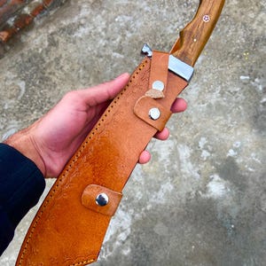 Close-up of polished rosewood handle on handmade carbon steel machete with ergonomic design.