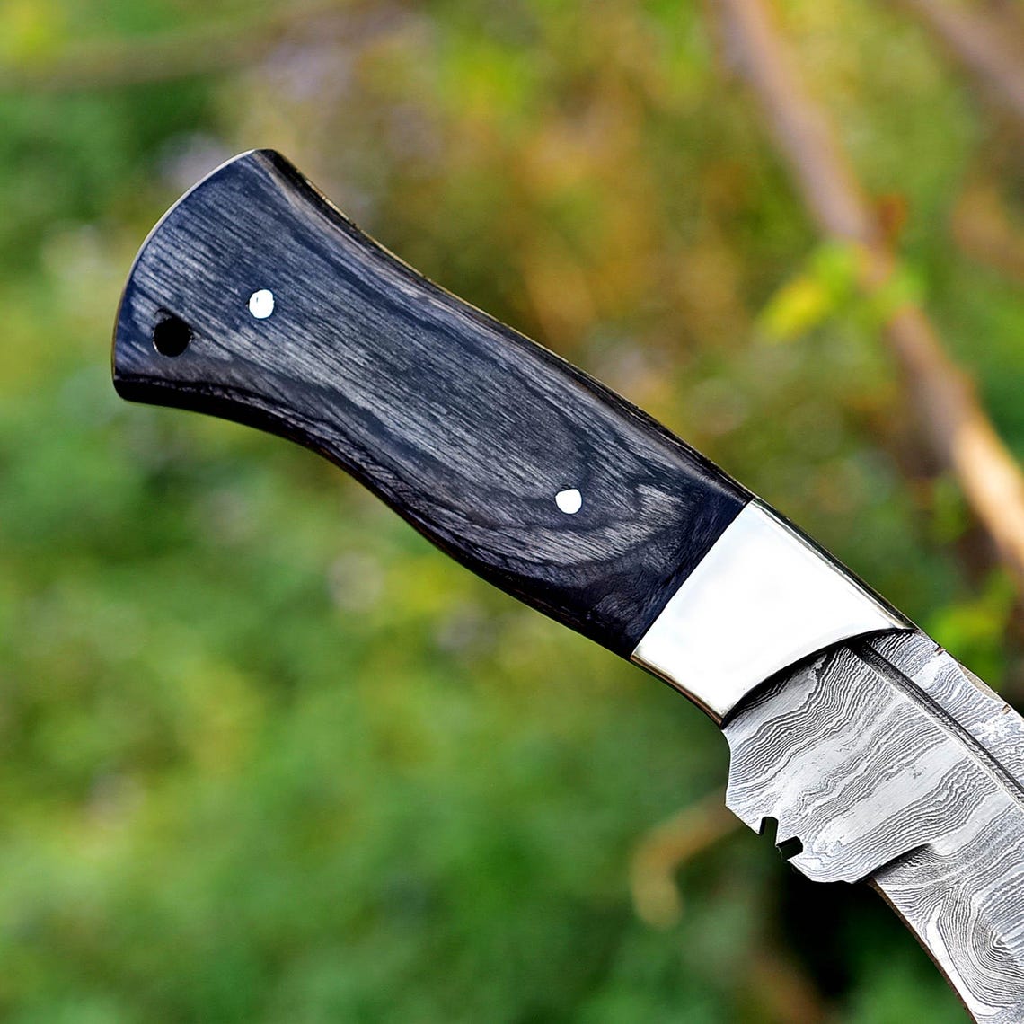 Full tang handmade Damascus Kukri knife displayed outdoors with Micarta handle, offering strength, grip, and durability for camping and hunting.
