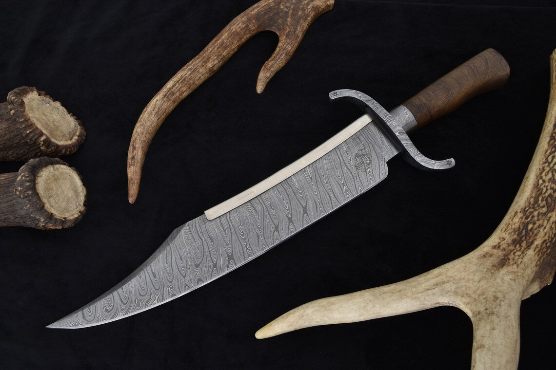 Handmade Damascus Texas Bowie knife featuring a large 14-inch blade with layered Damascus steel pattern, walnut wood handle, and forged guard. Comes with a custom wooden scabbard wrapped in leather. Perfect for collectors, hunters, and outdoor enthusiasts looking for a powerful handmade knife.