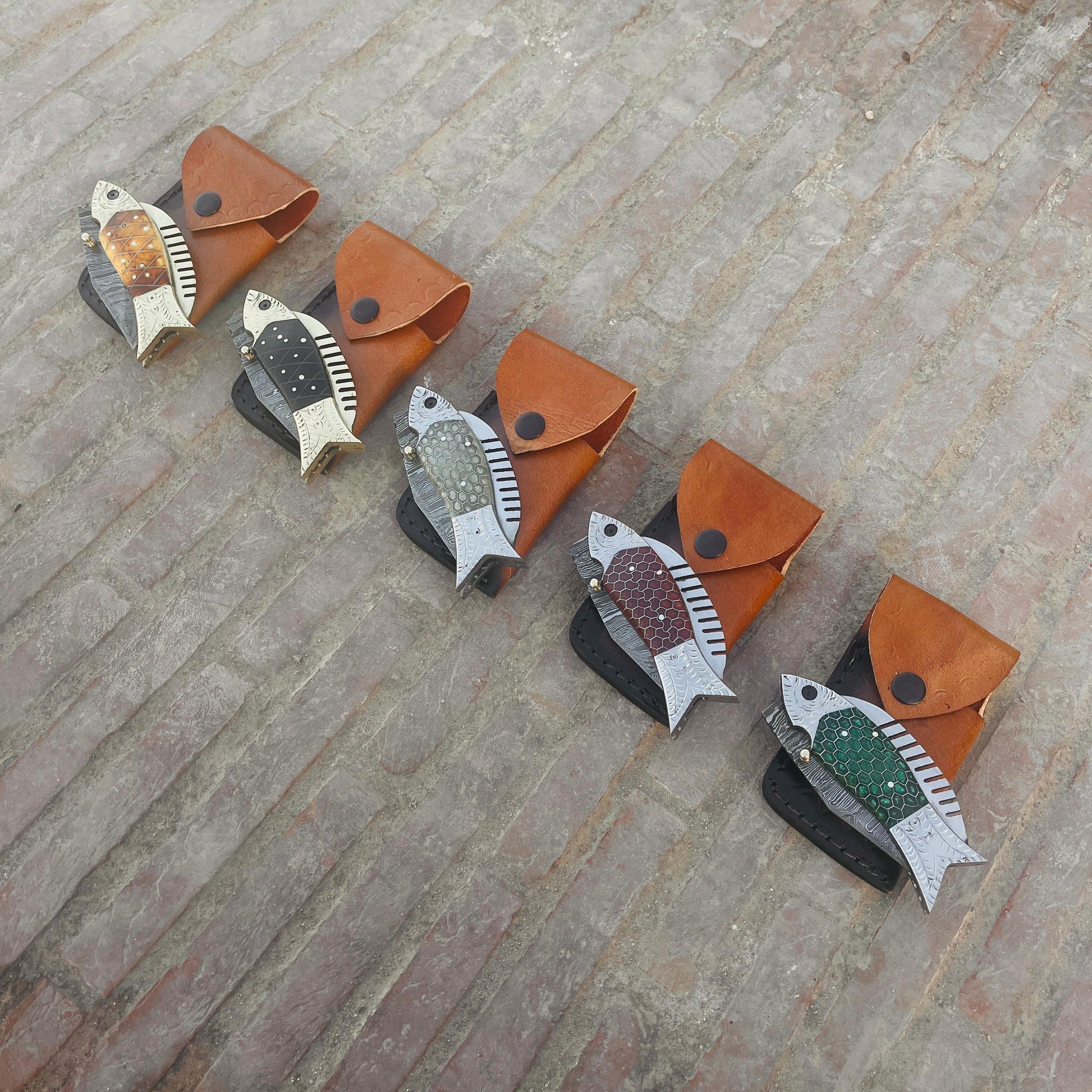 Multi color fish Damascus pocket knife collection displayed with leather pouches highlighting available handle color options.