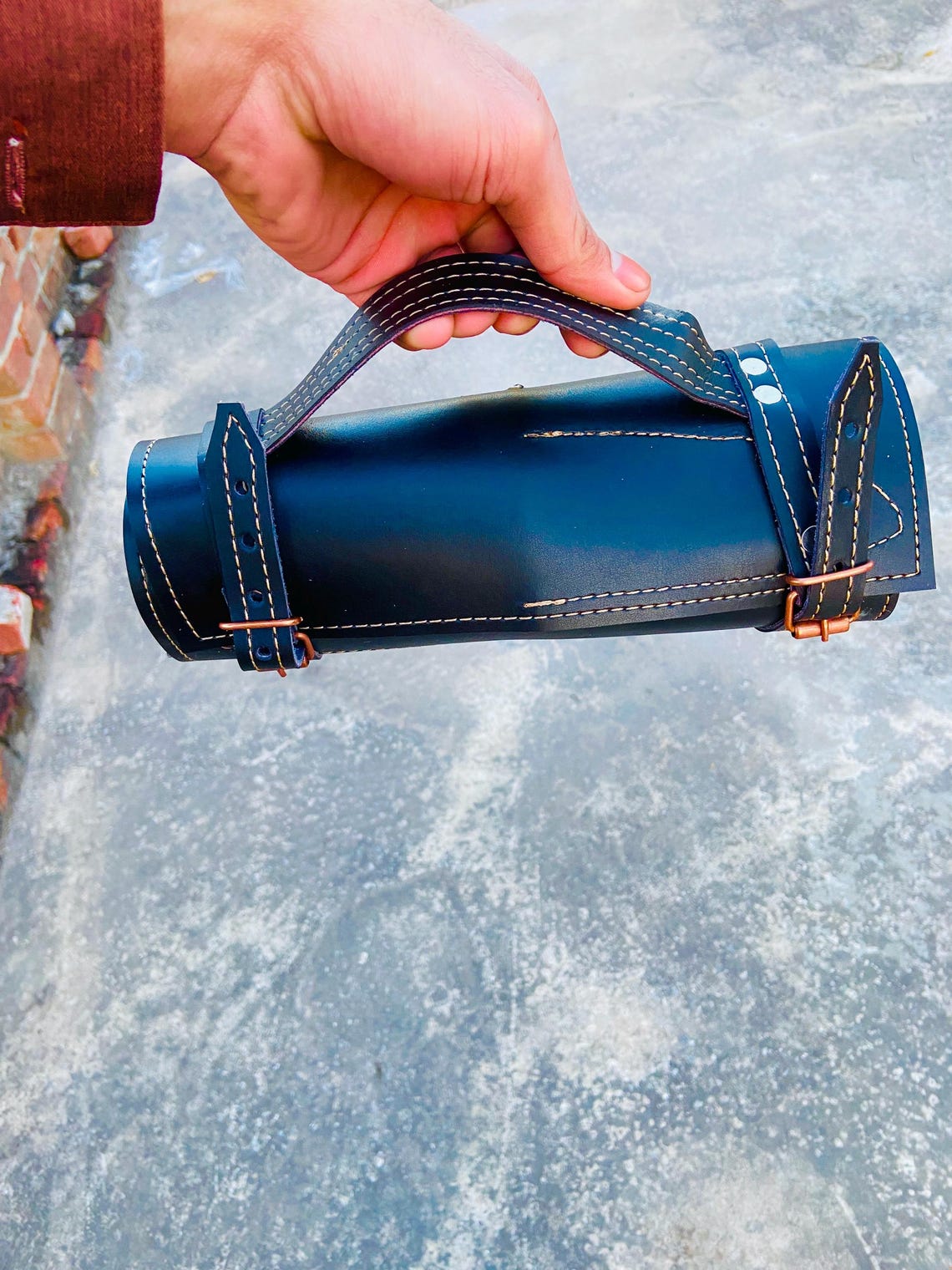 Close-up of handstitched black leather knife roll with handle and copper buckles.