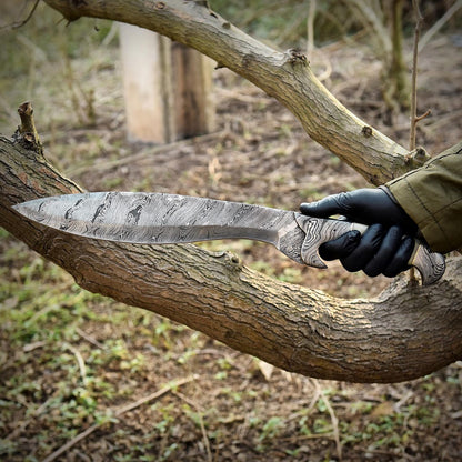 Handmade Damascus steel Kukri knife being held outdoors, showcasing ergonomic handle design, full tang construction, and polished blade pattern. Ideal for collectors and outdoor adventurers looking for a functional yet artistic survival knife.
