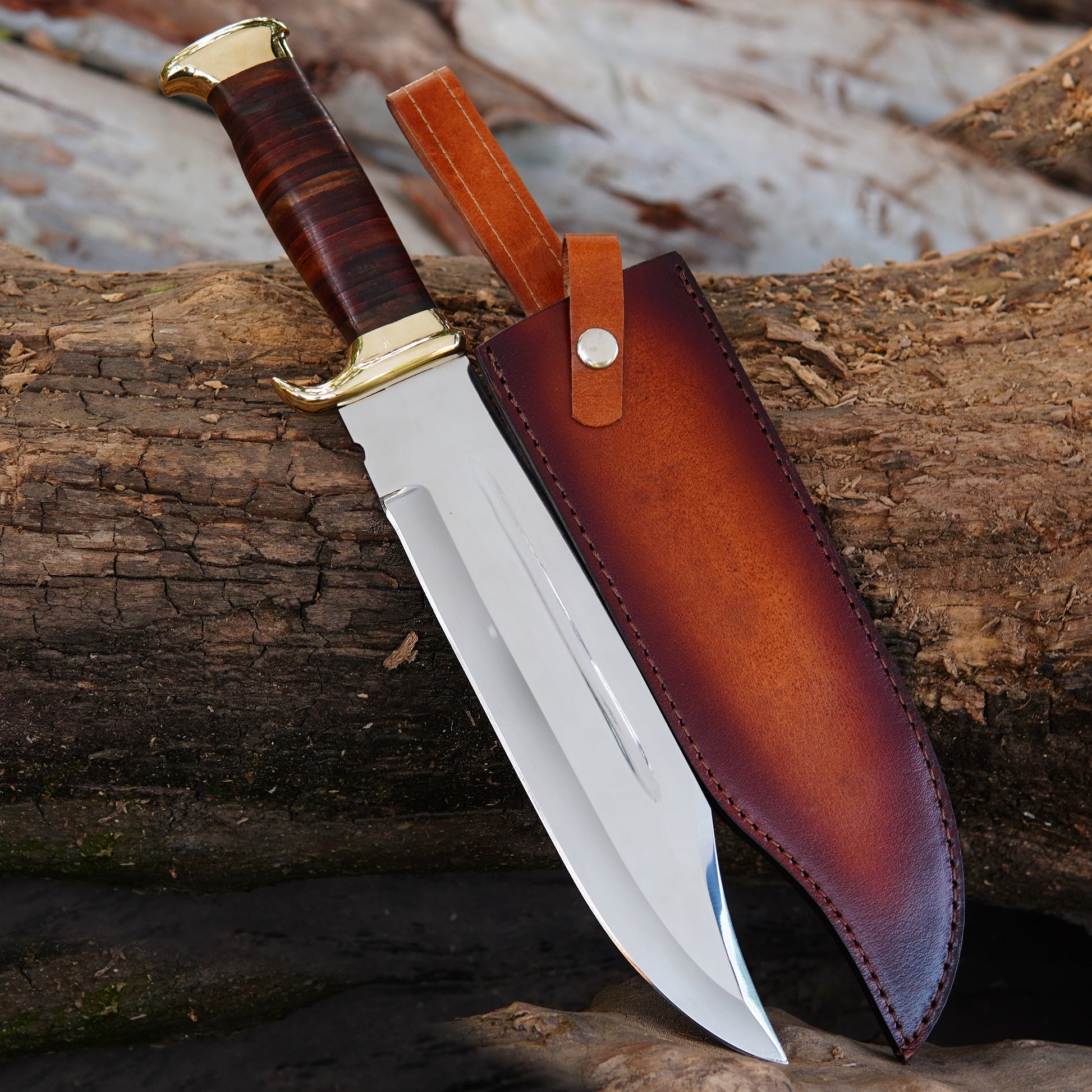 This handmade Bowie knife is displayed against stacked natural wood logs, highlighting its polished steel blade and rich brown stacked handle. The knife features a solid brass guard and pommel that add a premium, classic touch. The blade is sharpened and shaped for outdoor performance, making it ideal for camping, hunting, and survival use. The included pure leather sheath is designed for safe storage and easy carry, making this knife a perfect gift for him on birthdays, anniversaries, or special occasions.