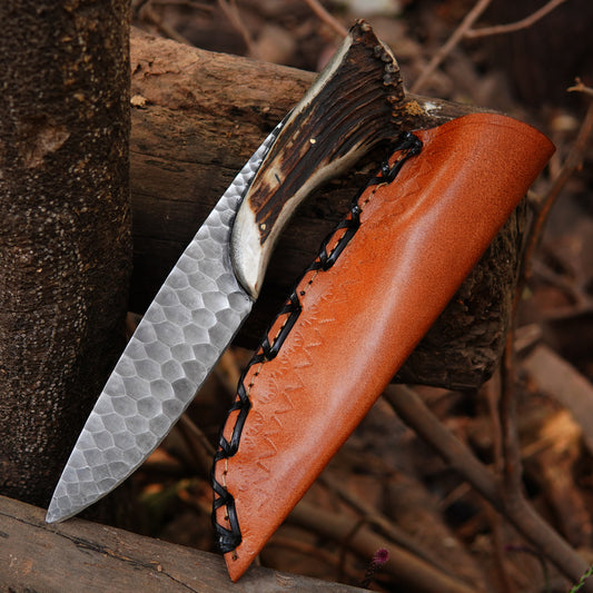 Handmade hunting knife with a hammered steel blade and natural material handle paired with a leather sheath.