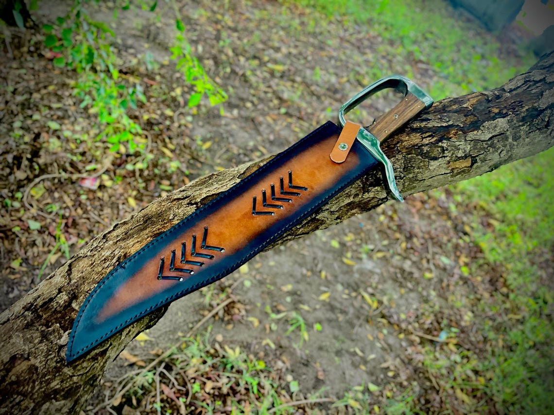 Handmade carbon steel Bowie knife with leather sheath lying on outdoor bench.