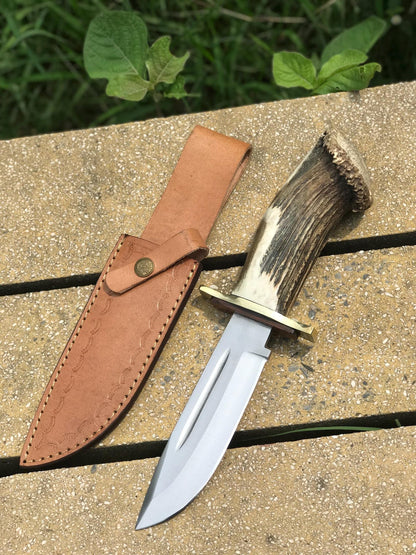 Stag handle carbon steel Bowie knife with hand-stitched leather sheath, designed for hunting, camping, and collection. Features a polished blade, brass guard, and comfortable grip — handmade for durability and style in outdoor conditions.