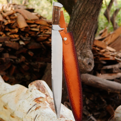 Handmade large bowie knife placed outdoors on wood logs featuring a long high carbon steel blade with sharp edge and strong full tang build. The natural wood handle shows rich grain patterns and ergonomic shaping for a comfortable grip. Designed for camping hunting and survival tasks this heavy duty knife comes with a pure leather sheath making it ideal for collectors outdoor enthusiasts and practical field use