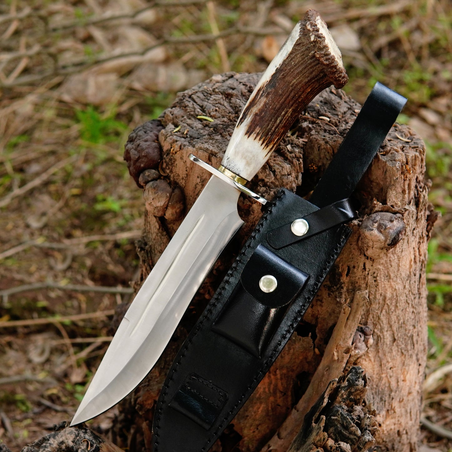 Handmade bowie hunting knife placed on a wooden log with premium black leather sheath showing sharp polished blade and natural textured handle, designed for outdoor camping survival hunting and bushcraft use with strong full tang construction and comfortable grip for everyday field tasks