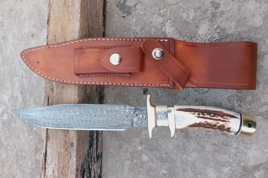 Custom Damascus steel hunting knife with brass guard, stag handle, and sharp patterned blade. Includes a durable hand-stitched sheath. Designed for outdoor use, hunting, and display in collections, balancing artistry with practical use.