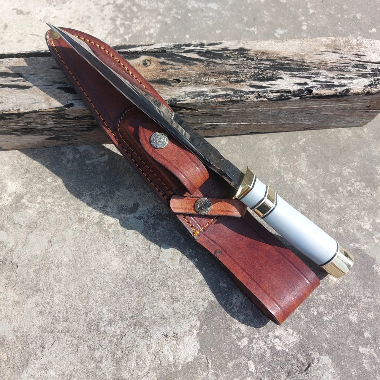 Elegant outdoor knife featuring a polished steel blade and smooth white handle with brass guard. Delivered with a stitched leather sheath, offering strength and style in one package.