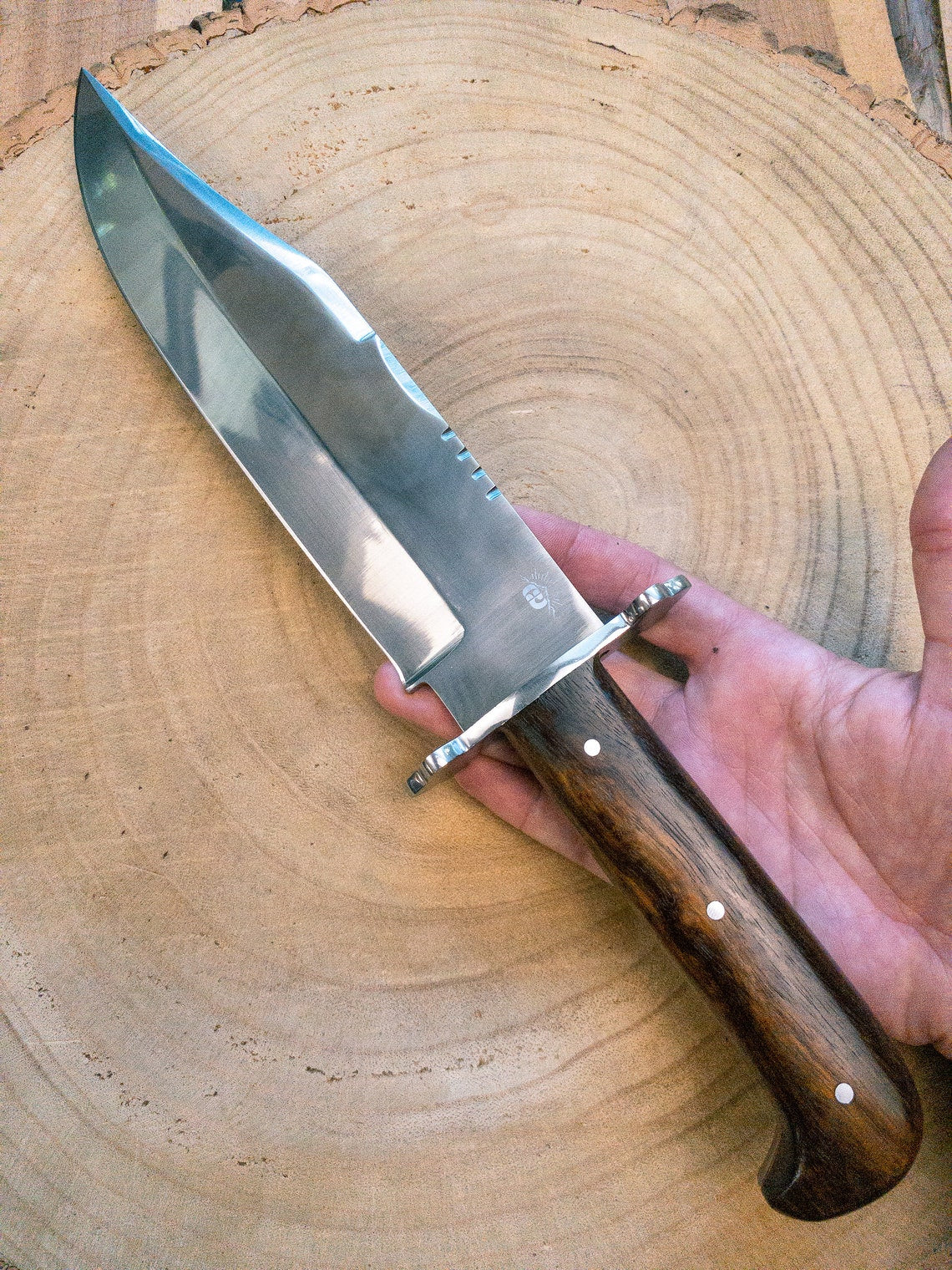 Handmade Bowie knife with carbon steel blade and full tang construction, polished to perfection. The natural wood handle ensures comfort and balance, making it ideal for collectors and adventurers alike.