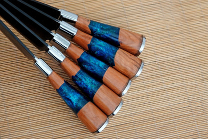 A 5 piece kitchen knife set handmade in black carbon steel with resin handles. Perfect for cutting, chopping, and cooking indoors or outdoors. Includes a leather sheath for safe storage and free engraving to make the set personal.