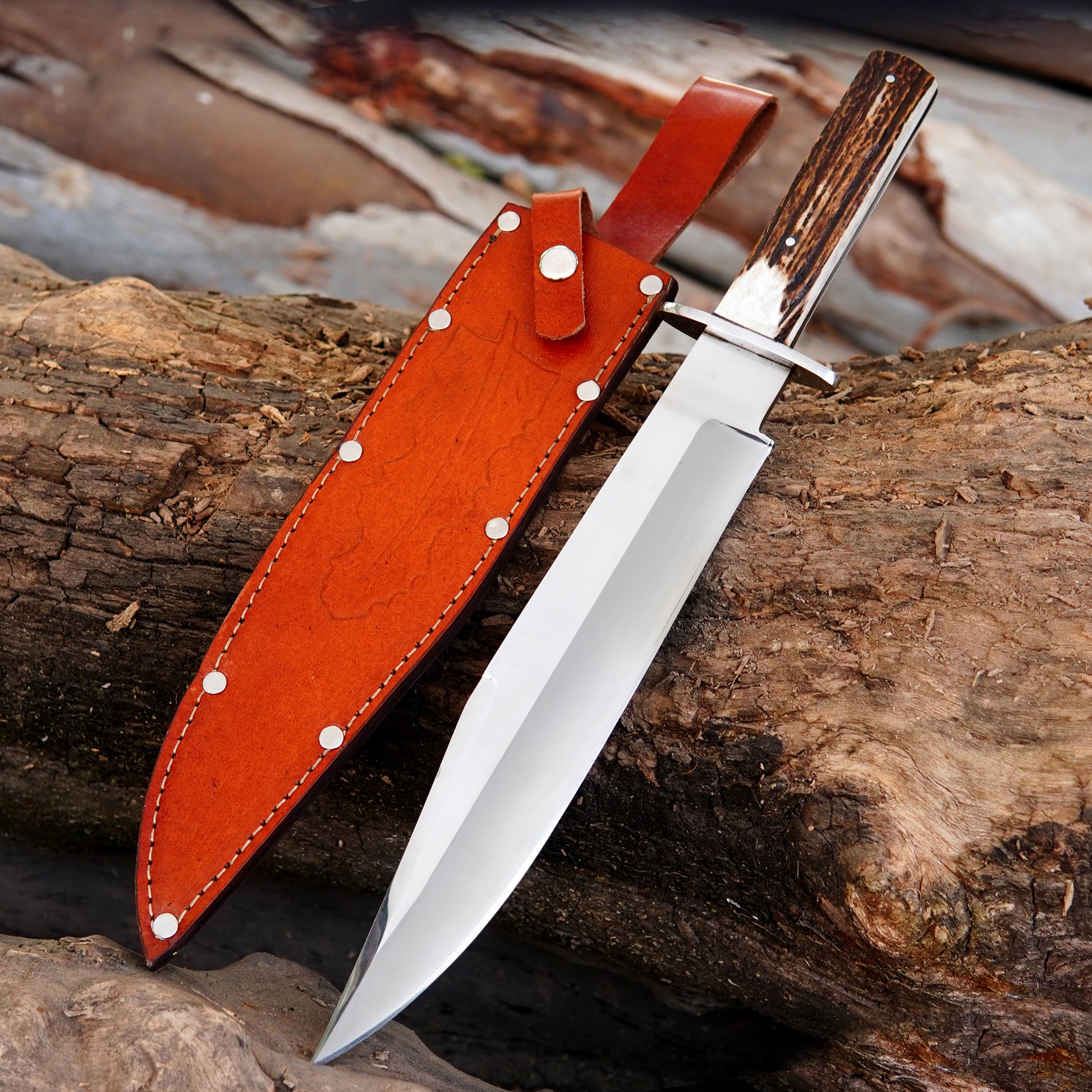 Handmade full tang Bowie knife with satin polished carbon steel blade displayed on rustic wooden logs.