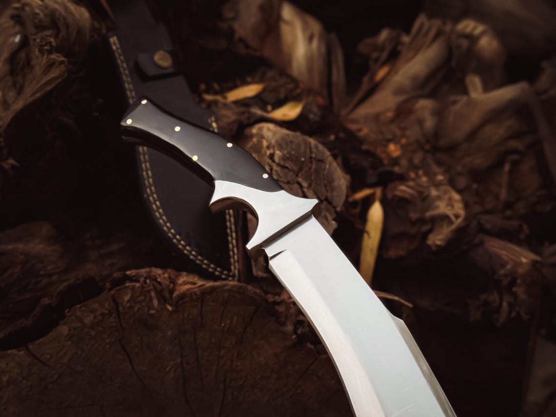 Knife held in hand demonstrating grip and scale against a natural wood background.