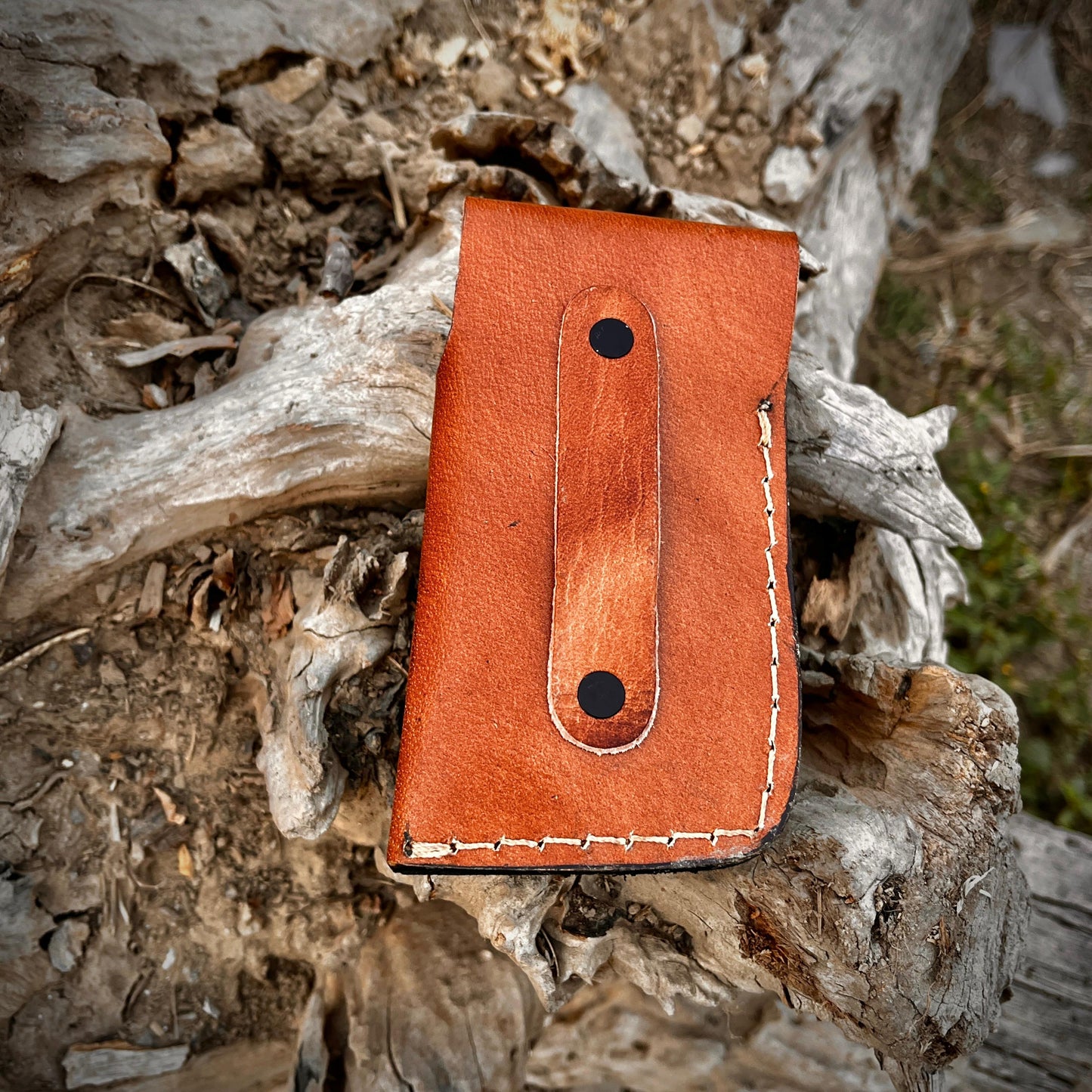 Outdoor photo of handmade fish shaped Damascus pocket knife placed on natural wood with leather sheath showing everyday carry design.