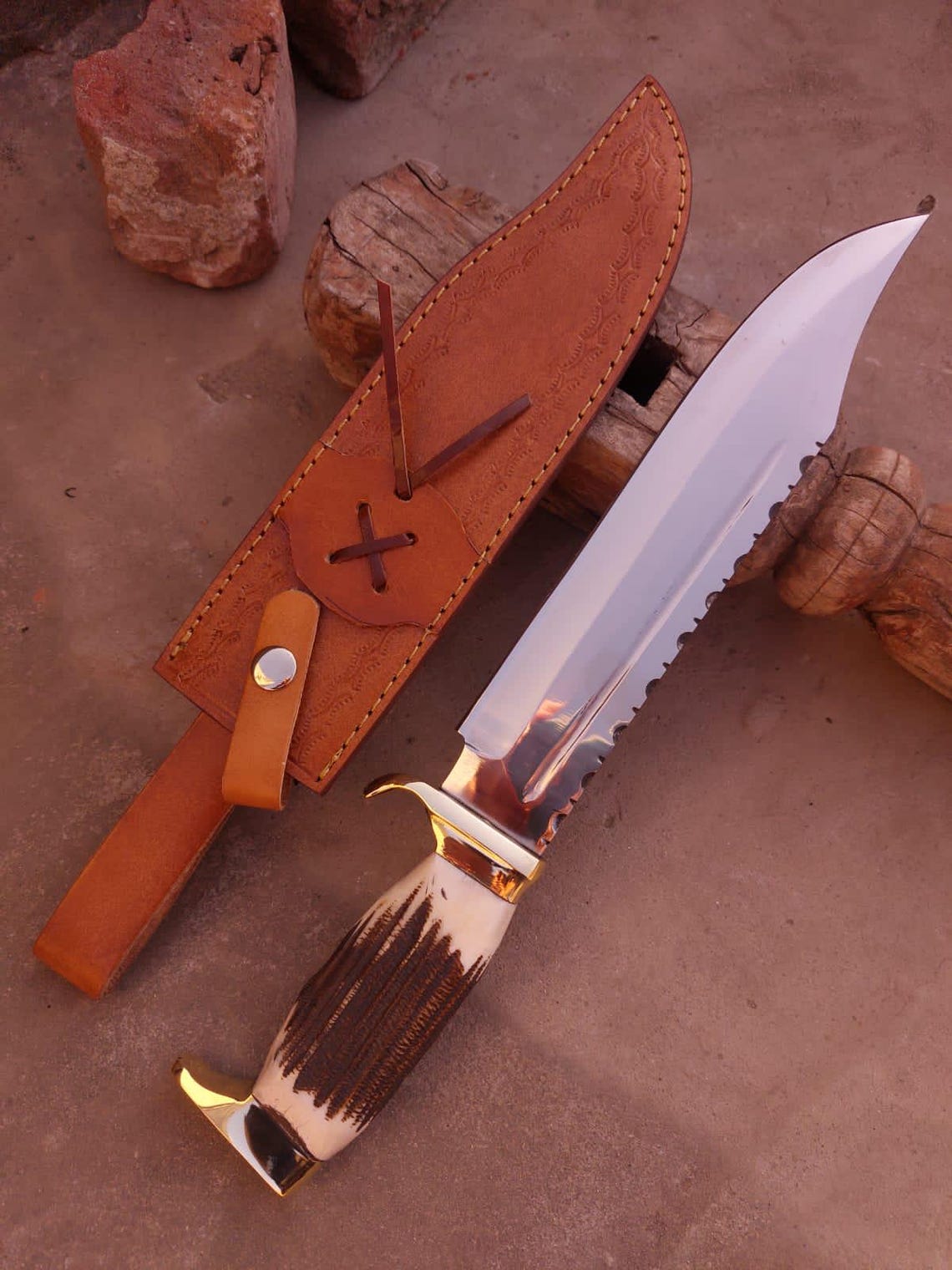 Bowie knife and sheath displayed on wooden block with natural light reflections on blade.