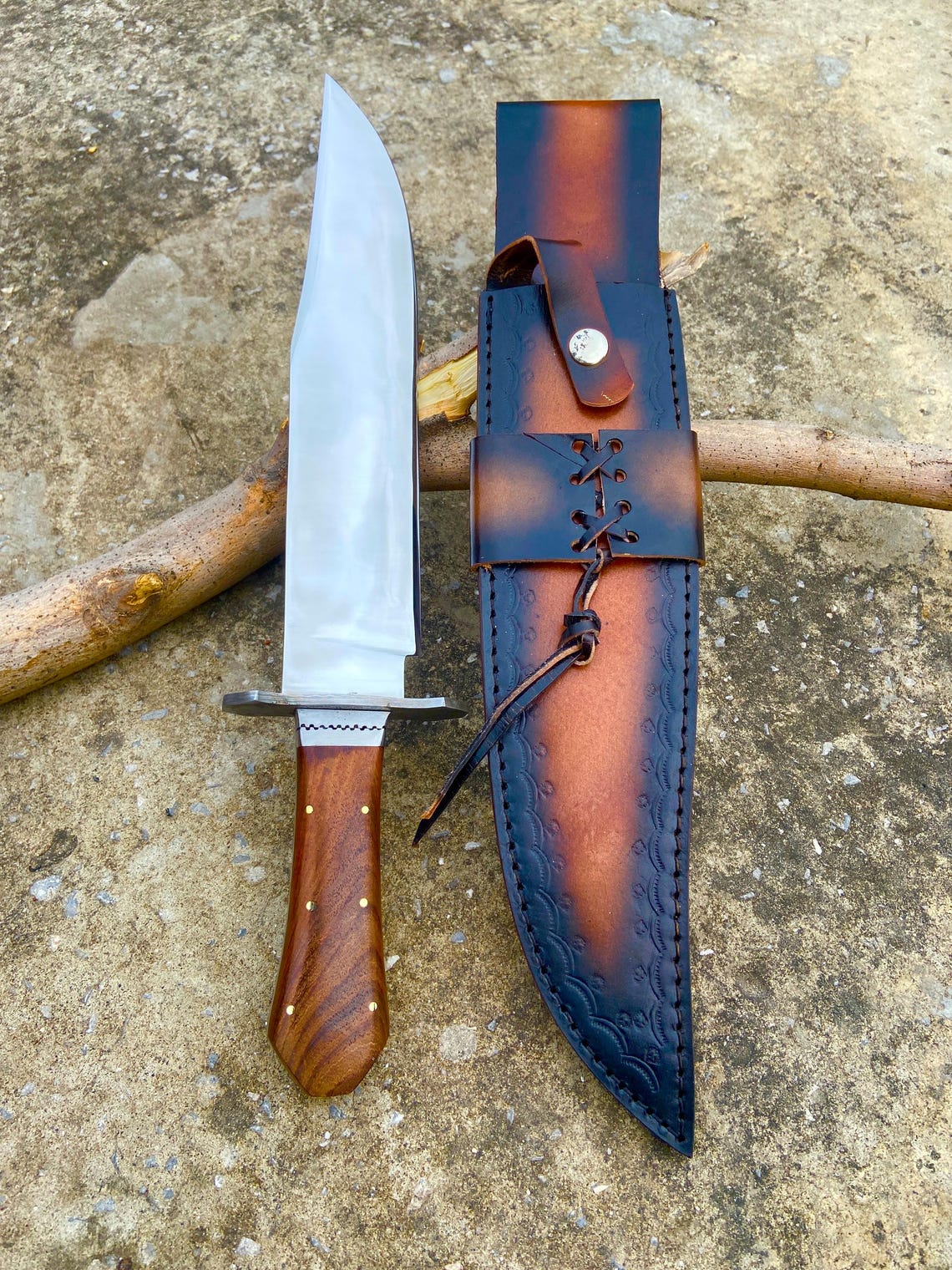 Polished carbon steel Bowie knife paired with a richly colored leather sheath featuring lace stitching. The rosewood coffin handle and steel guard blend strength with beauty. Designed for hunters, adventurers, and handmade knife collectors.