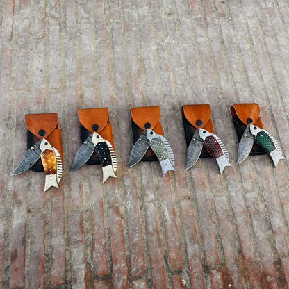 Close view of fish shaped Damascus pocket knife handle with honeycomb pattern and engraved metal details.