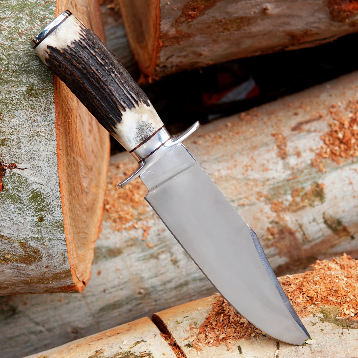 Close view of handmade bowie knife with leather sheath placed on wooden surface in outdoor environment. The image focuses on blade shape, handle texture, and natural outdoor presentation creating a strong visual appeal for buyers searching for a reliable outdoor knife or handcrafted gift option.