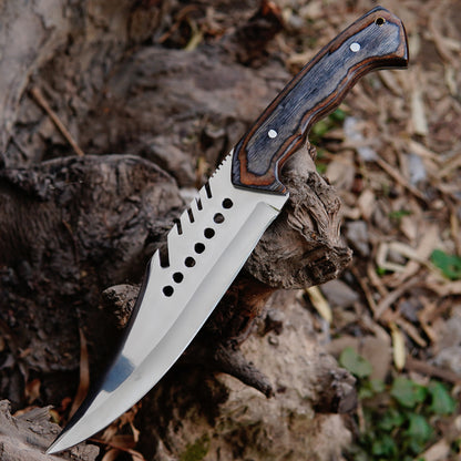 Close-up image of handmade bowie knife handle showing layered natural material texture and secure grip design. The photo focuses on the handle shape, metal pins, and smooth finishing that provides comfort during outdoor use. The leather sheath visible in the background adds a traditional and practical touch for safe storage and carrying.