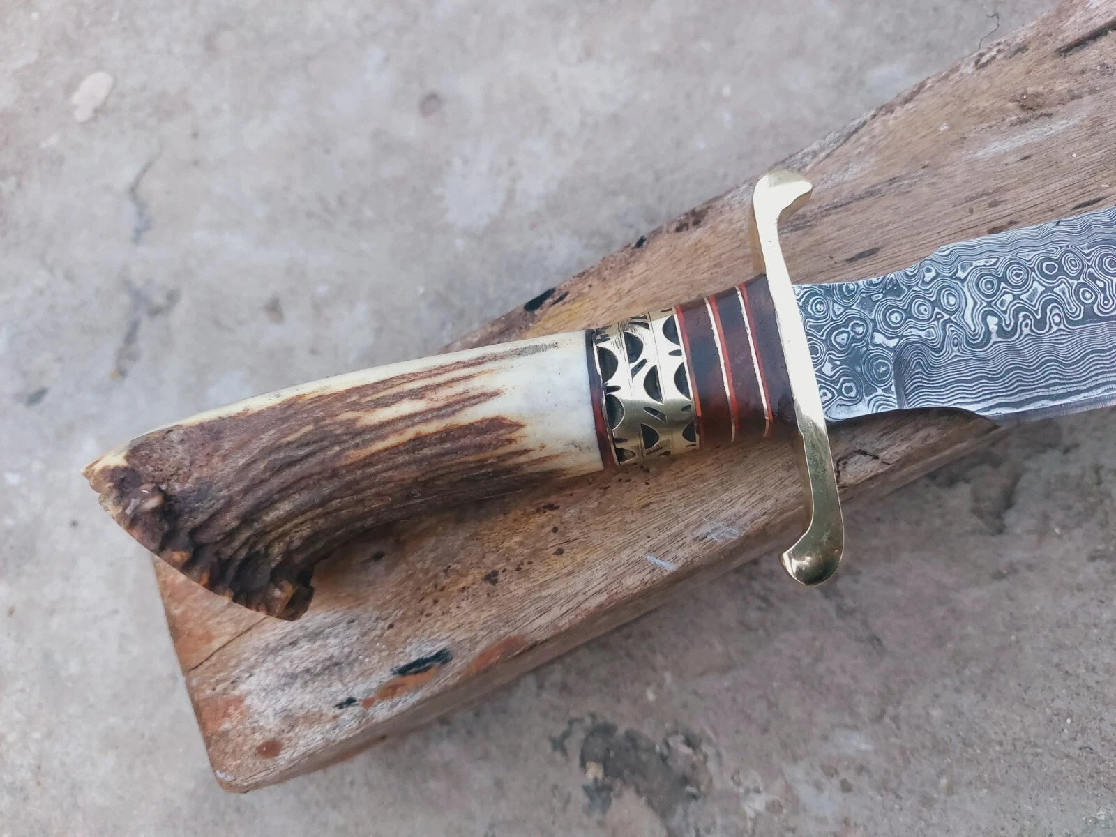 Damascus hunting knife with stag crown handle and brass spacer fittings. Each blade is hand-forged with unique Damascus steel patterns. Comes with a premium leather sheath, making it reliable for outdoor use, hunting, or as part of a knife collection.