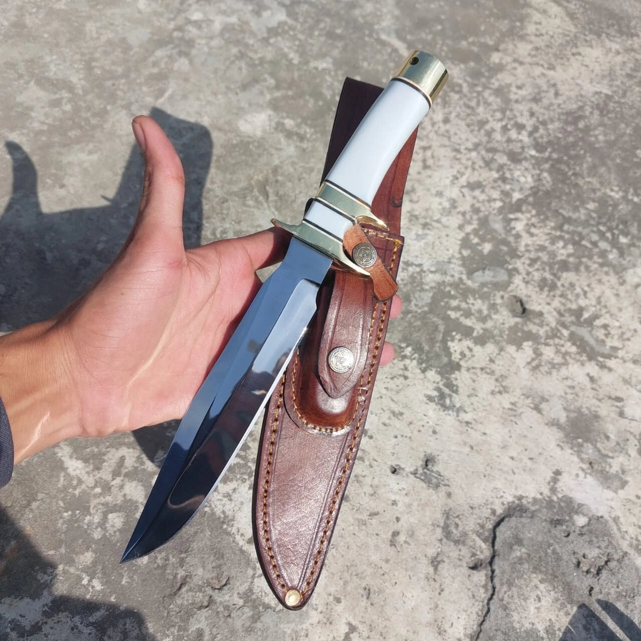 Handmade fixed blade hunting knife with polished finish, brass fittings, and a white handle grip. Accompanied by a stitched leather sheath, designed for reliable outdoor use.