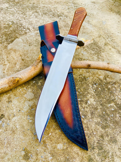 Top view of full-tang handmade carbon steel Bowie knife with rosewood handle and mirror finish blade. The leather sheath beside it shows detailed craftsmanship and secure fit. A collectible handmade knife ideal for outdoor enthusiasts.