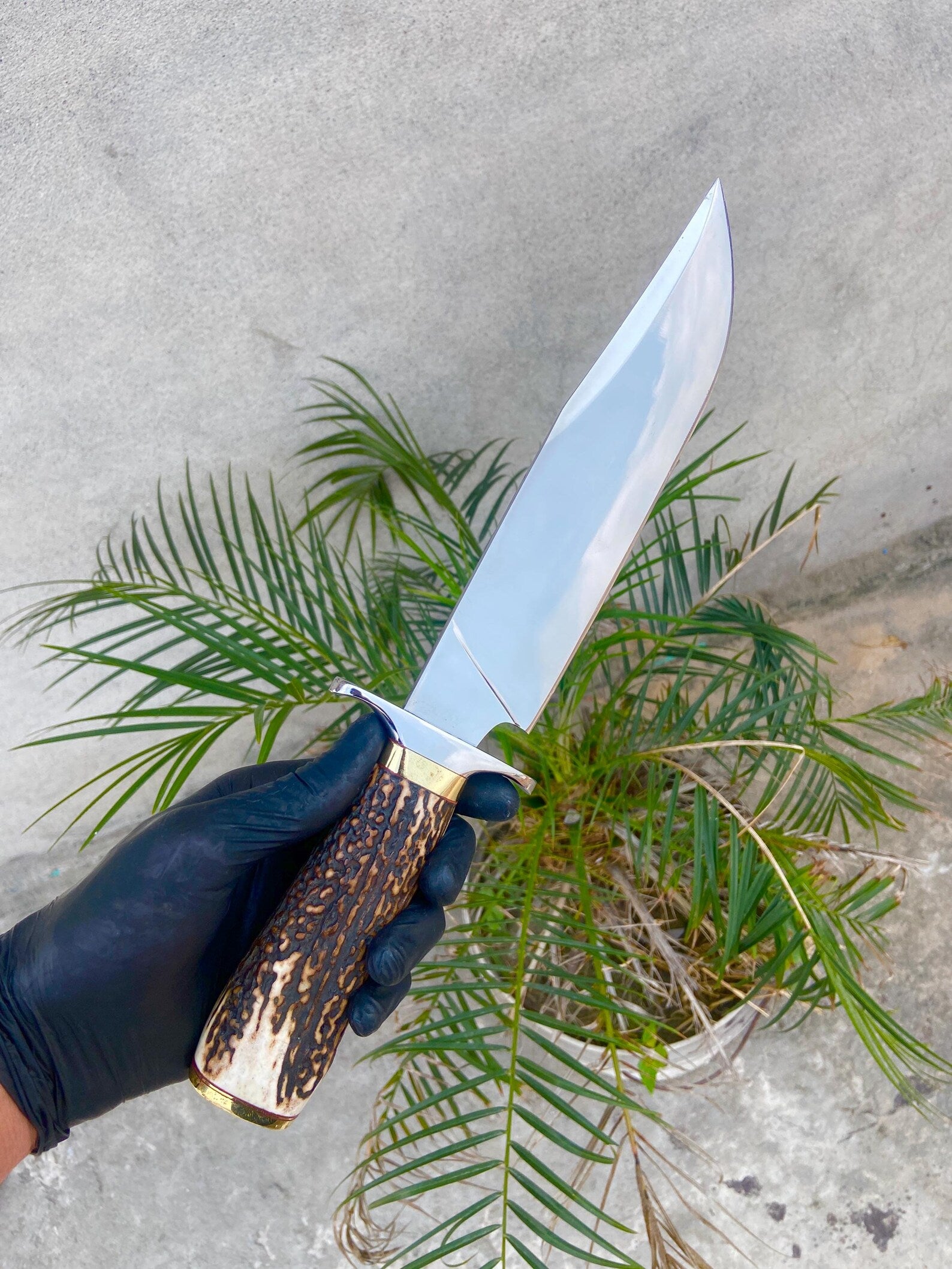 Handmade carbon steel Bowie knife with red-brown leather sheath, crafted for hunters and collectors.