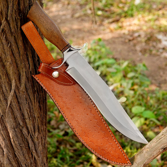 Handmade fixed blade hunting knife displayed outdoors on wood logs featuring a smooth wooden handle and polished high carbon steel blade designed for camping survival bushcraft and everyday outdoor cutting tasks with a secure leather sheath for easy belt carry