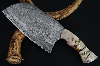 This outdoor Serbian knife is handmade from Damascus steel with a full tang cleaver blade and ram horn handle. Reliable for heavy chopping, BBQ prep, or camping. A unique piece that includes free custom engraving.