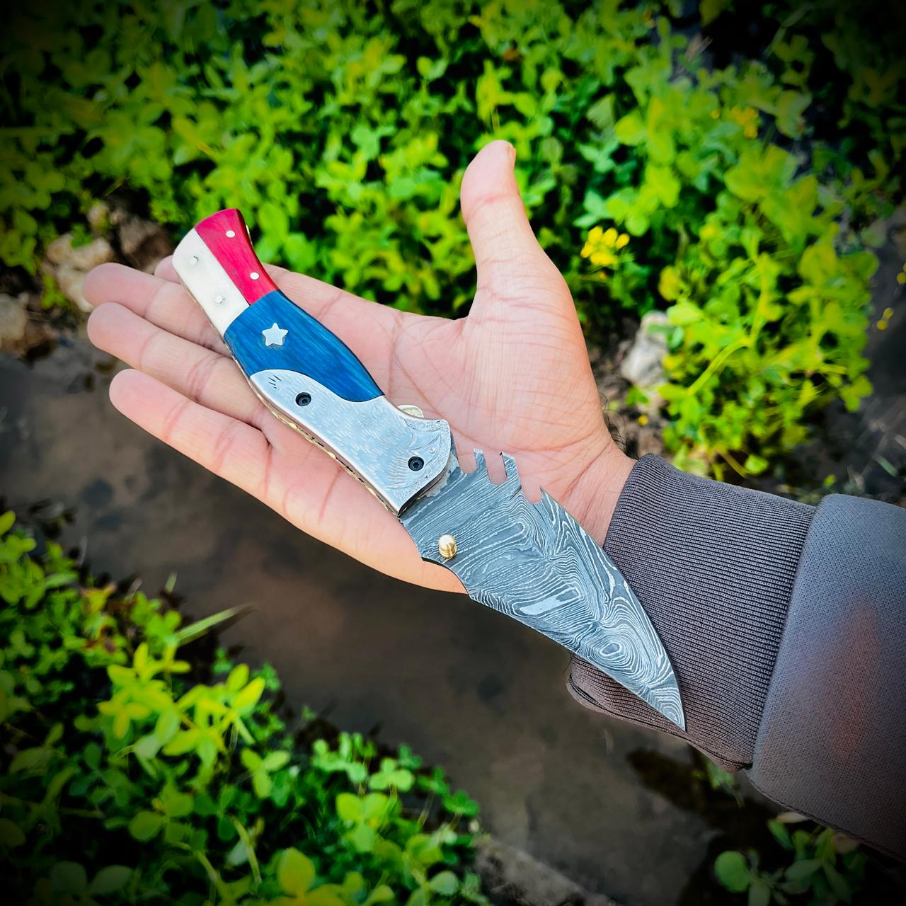 Close view of Damascus folding knife showing layered steel blade and red white blue handle design.