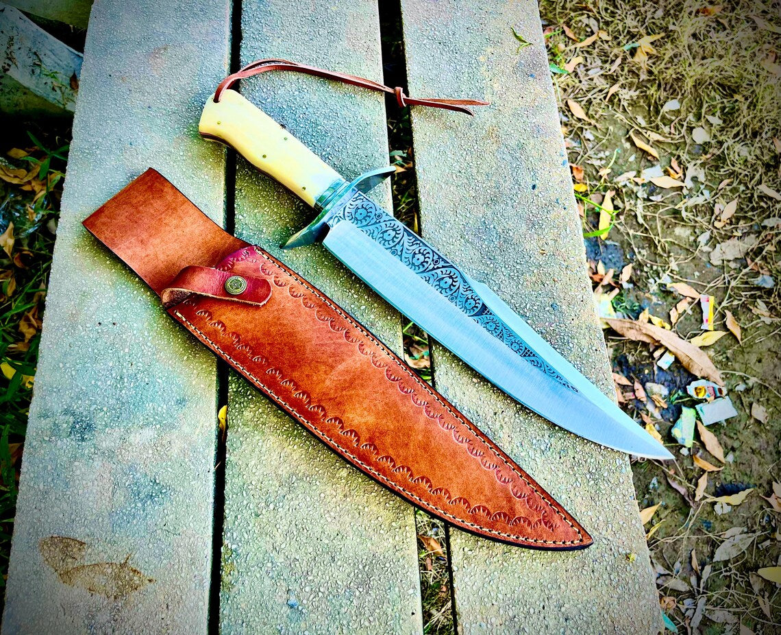 Engraved bowie knife set on outdoor bench with sheath and natural handle with lanyard attached.