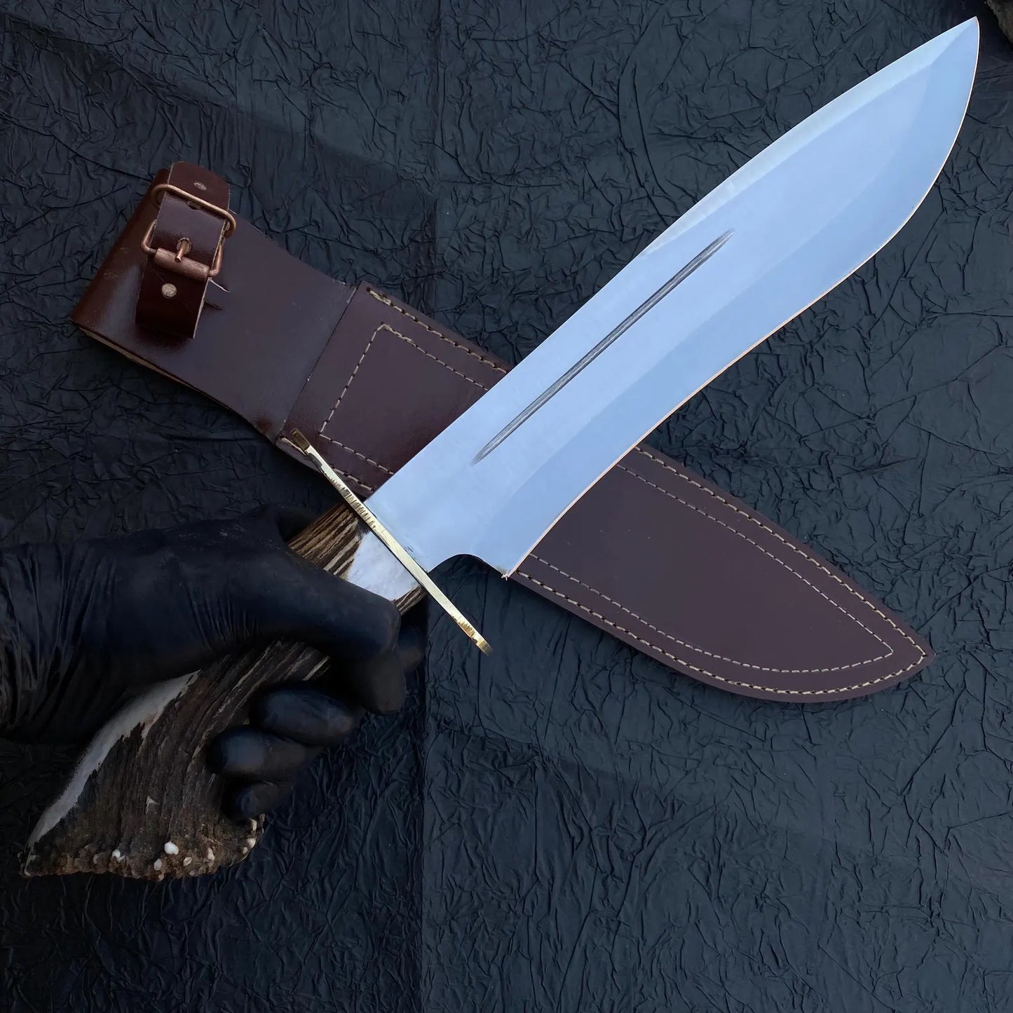 Close-up of custom Bowie knife showing detailed brass guard, handmade carbon steel blade, and antler crown handle.