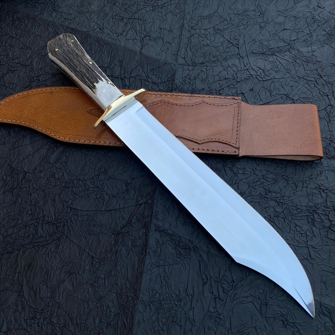Bowie knife resting on brown hand-stitched leather sheath.