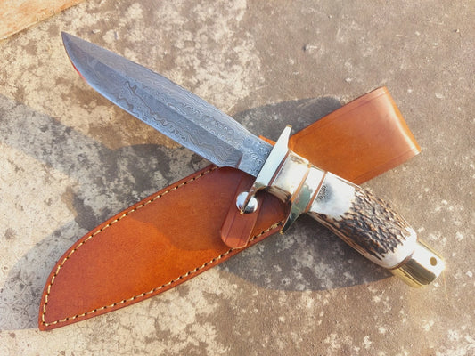 Handmade hunting knife featuring a damascus steel blade with a wave pattern, paired with a natural material handle for a secure grip. The knife includes a custom hand stitched leather sheath, making it ideal for collectors, hunters, and outdoor adventurers who appreciate craftsmanship and reliable performance. A unique handmade piece that balances functionality with traditional design.